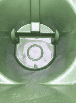 Close-up view of the inside of a green plastic trash bin, showing its circular base with a central ring pattern and hinge mechanism. The surface appears slightly worn and reflective, ideal for before-and-after shots by a trash can cleaning service. Close-up view of the inside of a green plastic trash bin, showing its circular base with a central ring pattern and hinge mechanism. The surface appears slightly worn and reflective, ideal for before-and-after shots by a trash can cleaning service.